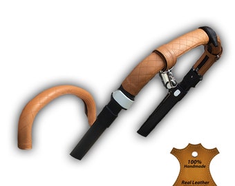 May include: Tan leather stroller handlebar covers with a quilted pattern. The covers are 100% handmade and made of real leather. The covers are attached to the stroller handlebar with a black strap and a silver buckle.