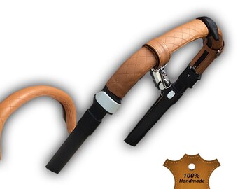 May include: Tan leather stroller handlebar cover with a quilted design. The cover is attached to the handlebar with a black strap and a silver buckle. The cover is made of 100% real leather and is handmade. The text on the leather tag reads "100% Handmade Real Leather Premium Quality".