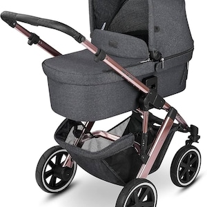 May include: A dark gray stroller with rose gold accents. The stroller features a canopy, a storage basket, and four wheels with white trim. The handle is black. The brand name "ABC Design" is visible on the side.