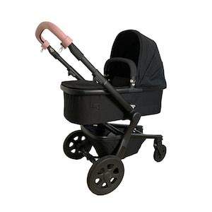May include: A black stroller with a pink leather handle and a black fabric canopy. The stroller has a black basket underneath and four black wheels.