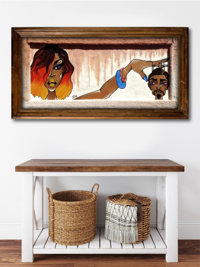 May include: A framed painting depicting a woman with red and orange hair holding a string attached to a man's head. The woman is wearing a blue bracelet and has blue nail polish. The man is wearing a black and white striped shirt and has a black beard. The background is a light brown colour.