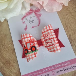 May include: Red and white gingham hair bow with a red tractor and the text "Just a girl who loves tractors!"