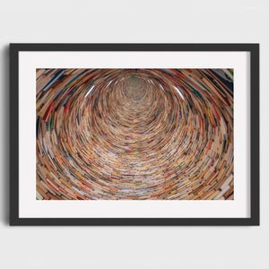 May include: A framed print featuring a tunnel-like composition created from the spines of numerous books. The books' pages and covers display a variety of colors, creating a swirling, textured effect. The artwork is framed in a black border.