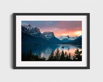 May include: A framed landscape photograph captures a serene mountain lake scene at sunset. The sky transitions from pink and orange to blue, reflecting in the calm water. Snow-capped mountains and evergreen trees frame the lake.