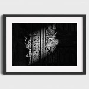 May include: Black and white framed print of ancient Egyptian hieroglyphs carved into stone. The image is dramatically lit, with a spotlight effect highlighting the intricate details of the carvings and textures.