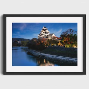 May include: A framed print of a Japanese castle at dusk. The castle is white and black with multiple tiers, set against a blue sky. A body of water reflects the castle and the surrounding trees.