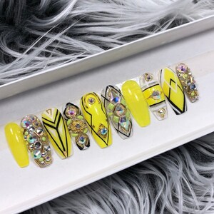 May include: A set of ten yellow press-on nails with black and white geometric designs and rhinestones.