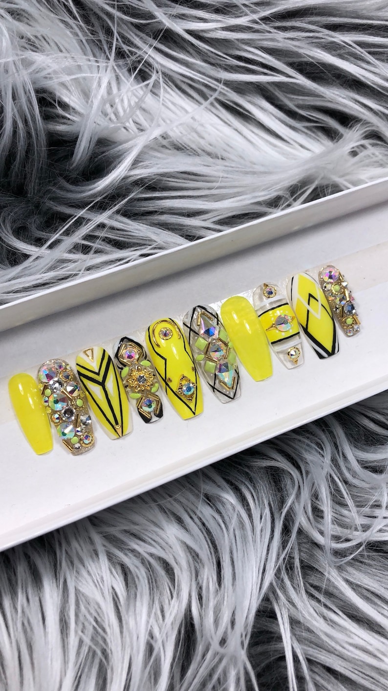 May include: A set of ten yellow press-on nails with black and white geometric designs and rhinestones.