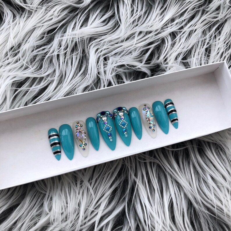 May include: Set of ten teal blue stiletto false nails with rhinestones and black and white stripes.
