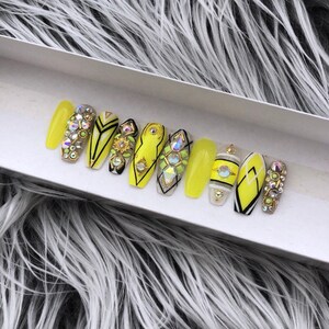 May include: A set of ten yellow press-on nails with black and white geometric designs and rhinestones.