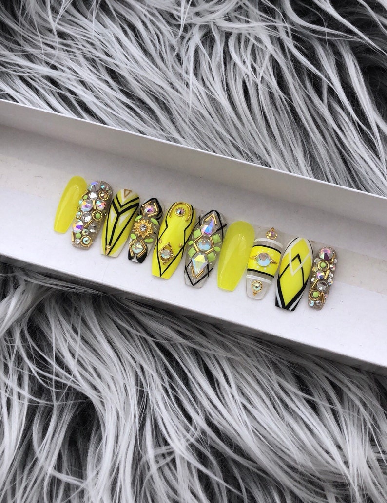 May include: A set of ten yellow press-on nails with black and white geometric designs and rhinestones.