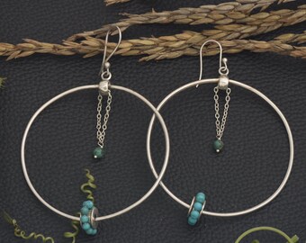 May include: A pair of silver hoop earrings with turquoise beads. The hoops are large and have a delicate chain dangling from the top with a turquoise bead at the end.