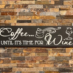 May include: Black wooden sign with white text that reads "Coffee... Until it's time for Wine". The sign features a white silhouette of a coffee cup with steam and a wine glass.