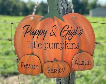 Puede incluir: Un letrero de madera en forma de calabaza con el texto "Pappy & Gigi's little pumpkins" y tres calabazas más pequeñas con los nombres "Peyton", "Paisley" y "Austin" escritos en ellas.