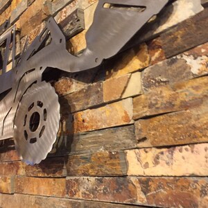 May include: A metal silhouette of a tractor mounted on a stone wall. The tractor is made of brushed metal and has a detailed design.