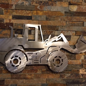May include: A metal silhouette of a front loader excavator, painted in a silver finish, mounted on a brick wall.