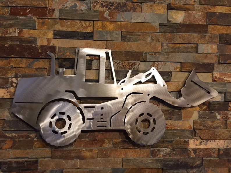 May include: A metal silhouette of a front loader excavator, painted in a silver finish, mounted on a brick wall.