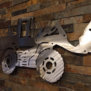 May include: A metal wall sculpture of a front loader, a type of construction equipment, with a silver finish. The sculpture is mounted on a brick wall.