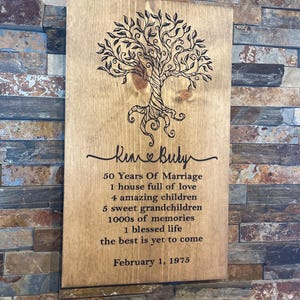 May include: A wooden sign with a tree design and the text "Kim & Buly 50 Years Of Marriage 1 house full of love 4 amazing children 5 sweet grandchildren 1000s of memories 1 blessed life the best is yet to come February 1, 1975"