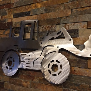 May include: A metal silhouette of a front loader, a type of construction equipment, mounted on a wall. The silhouette is made of brushed stainless steel and has a detailed design.