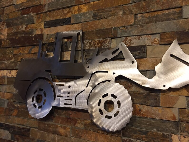 May include: A metal silhouette of a front loader, a type of construction equipment, mounted on a wall. The silhouette is made of brushed stainless steel and has a detailed design.