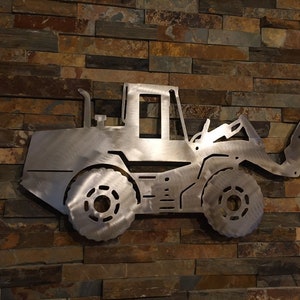 May include: A silver metal cutout of a front loader, a type of construction equipment, mounted on a brick wall.