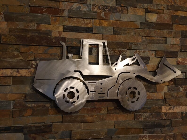 May include: A silver metal cutout of a front loader, a type of construction equipment, mounted on a brick wall.