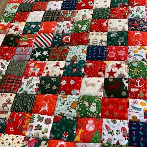 May include: A patchwork quilt with a festive Christmas theme. The quilt is composed of numerous fabric squares in red, green, white, and navy blue. Each square features holiday-themed patterns, including reindeer, snowmen, and Christmas trees.
