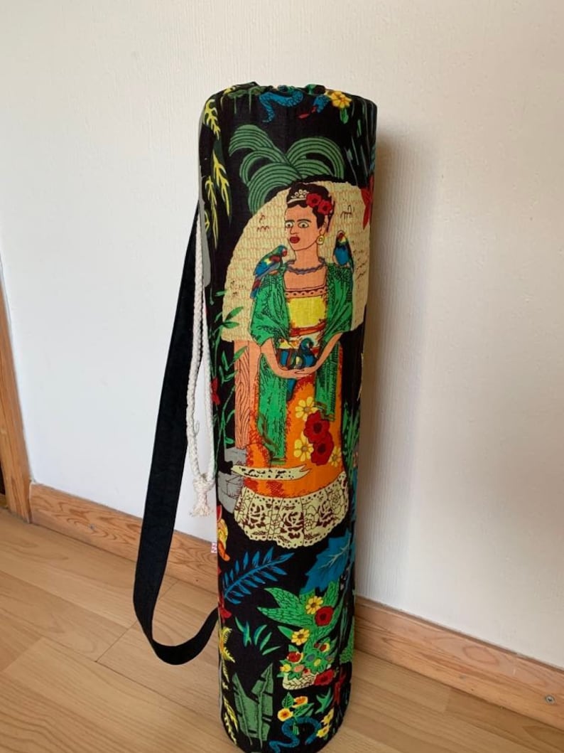 May include: Black yoga mat bag with a colorful print featuring a woman with flowers and birds. The bag has a drawstring closure and a black strap.