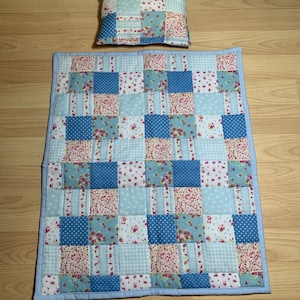 May include: A blue and pink patchwork quilt with a matching pillow. The quilt is made of squares of different fabrics with floral and geometric patterns.