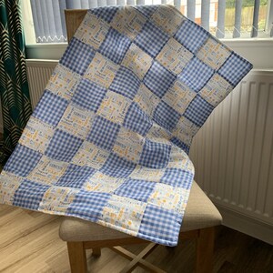 May include: A blue and white gingham baby blanket with a patchwork design featuring yellow text that says "Circus" and "Lion".