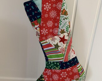 May include: A Christmas stocking constructed from various fabric patches featuring festive patterns including red snowflakes, green holly, striped ribbons, and stars. The stocking is suspended by a thin red cord and displays a colorful patchwork design.