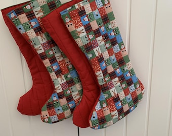 May include: Two Christmas stockings featuring a patchwork pattern of festive icons including Santa Claus, reindeer, snowmen, and plaid squares. The stockings have solid red fabric backs and red ribbon loops for hanging, with a multi-colored front design.