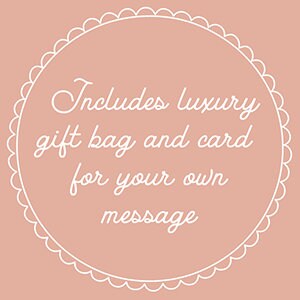Puede incluir: Un c&iacute;rculo blanco con un borde festoneado sobre un fondo rosa claro. El texto "Includes luxury gift bag and card for your own message" est&aacute; escrito en blanco en cursiva.