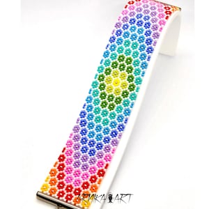 以下が含まれることがあります： 小さな多色のビーズを六角形のフラワーパターンで並べた幅広のブレスレット。赤、オレンジ、黄色、緑、青、紫と虹色のスペクトルで色が変化しています。ARNIKA ARTという文字がプリントされています。