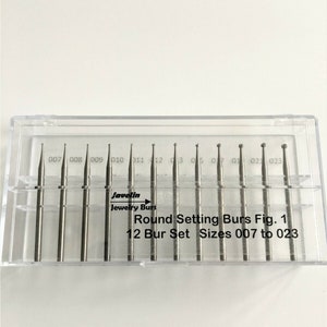 May include: A clear plastic case containing a set of 12 round setting burs for jewelry making. The burs are silver-colored and range in size from 007 to 023. The case has the text "Javelin Jewelry Burs" and "Round Setting Burs Fig. 1".
