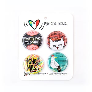 May include: Four round pinback buttons with colourful designs. The top left button has a pink and red brain with the text "Worry pas ta brain!" in black. The top right button has a white cat with a grumpy expression and the text "J'care pas qare pas-J'care" in black. The bottom left button has a colourful abstract design with the text "Tcheu Mess" in black. The bottom right button has a blue and green seagull with a red hat and the text "Caraquet" in black.