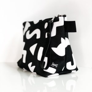 May include: Black and white geometric patterned zippered makeup bag with a black leather strap and the word "Jaws" written in white on the front.