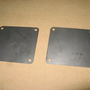 May include: Two metal plates with rounded corners and four holes each. The plates are gray and have some scratches on the surface.