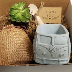May include: A gift box filled with a small succulent plant, a burlap bag, a wooden spoon, a blue ceramic planter shaped like a vintage Volkswagen van, and a small brown card with the text "Thank You".