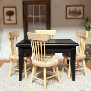 May include: Miniature dining room set with a black table and four light wood chairs. The chairs have a spindle back design. The room includes framed artwork and a neutral rug.