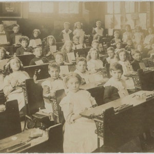 Ancienne photo de classe, lieu inconnu, années 1900-1910, vraie carte postale avec photo, enfants à un bureau, tenant des photos, salle de classe