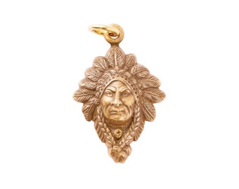 May include: Gold-toned pendant featuring a detailed relief of a Native American man's face wearing a headdress. The pendant has a loop at the top for attaching to a chain.