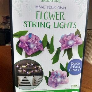 May include: Crayola Signature Make Your Own Flower String Lights craft kit. The box shows a purple flower with green leaves and a string of lights. The kit includes 4 sheets of leaves and paper flower bases, 1 roll of glue dots, 1 sheet of reinforcements, 2 dual-ended markers, 1 5 ft (1.5 m) 13 LED light strand, and 3 sheets of paper flower petals.