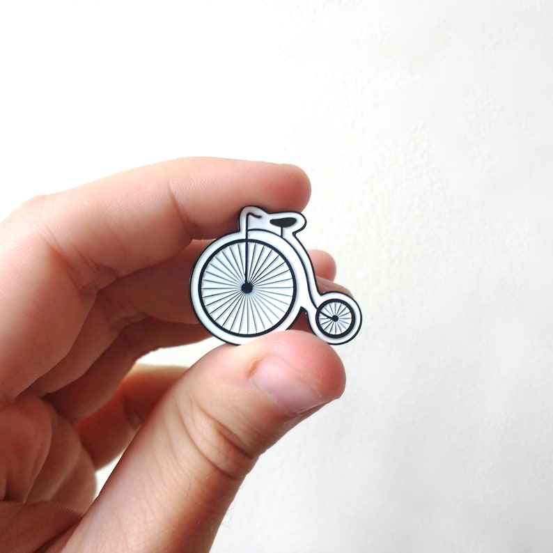 A hand holding the penny farthing pin, showing that it is not much bigger than the first knuckle of an adult thumb.