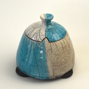 May include: A ceramic dome-shaped lidded box with a white and turquoise glaze. The box has a crackled glaze finish and sits on four small feet.