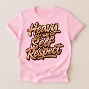 Puede incluir: Camiseta rosa claro con mangas enrolladas. La camiseta presenta la frase "Heavy on the Self Respect" en una fuente marr&oacute;n estilizada con contorno dorado. El texto est&aacute; centrado en la parte delantera.