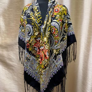 Può includere: Uno scialle nero con un motivo floreale nei toni del rosso, giallo e bianco. Lo scialle ha un bordo paisley viola e bianco ed è rifinito con frange nere.