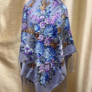 Può includere: Uno scialle quadrato lilla chiaro con un motivo floreale nei toni del blu, viola e marrone. Lo scialle ha un bordo con frange. Il motivo floreale presenta grandi fiori simili a peonie e fiori più piccoli. Accessorio tradizionale.