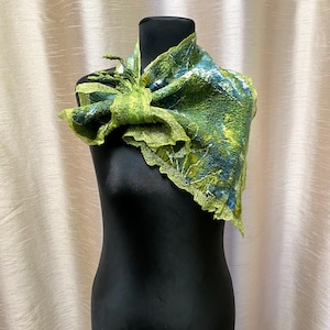 May include: A green and blue felted wool scarf displayed on a black mannequin. The scarf features a textured design with shades of green and blue, and a decorative knot. The edges have a delicate, ruffled trim.